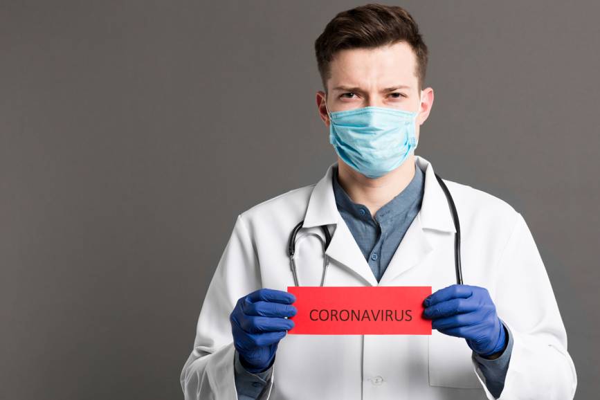 Lekarz z maseczką i  niebieskich rękawiczkach trzymający kartkę z napisem CORONAVIRUS