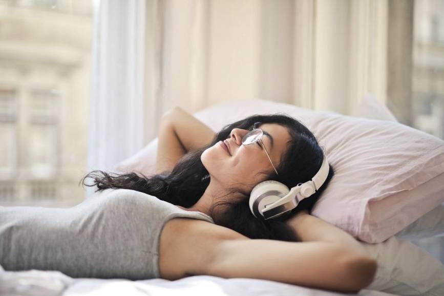 Zdjęcie przedstawia kobietę leżącą w łóżku ze słuchawkami na głowie