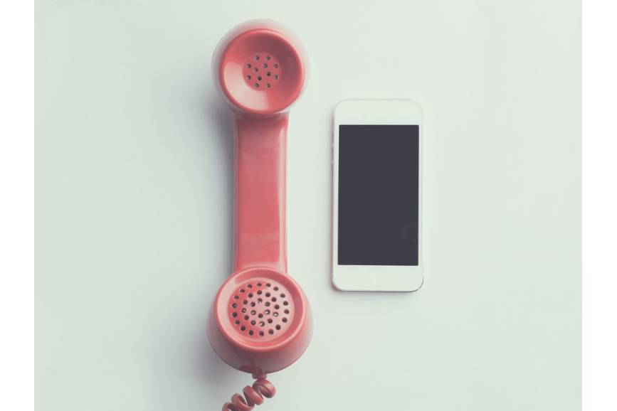 Zdjęcie przedstawia czerwoną słuchawkę od starego telefonu oraz nowoczesny smartfon