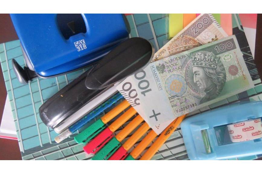 Zdjęcie przedstawia przybory szkolne oraz dwa banknoty, jeden stuzłotowy i drugi dwustuzłotowy 