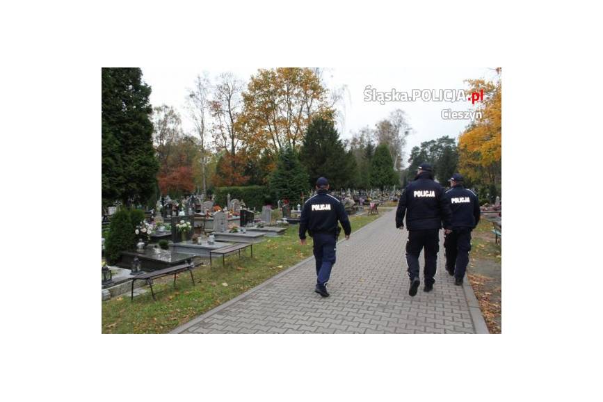 Dzień, trójka policjantów spaceruje po rejonie cmentarza, widoczne nagrobki