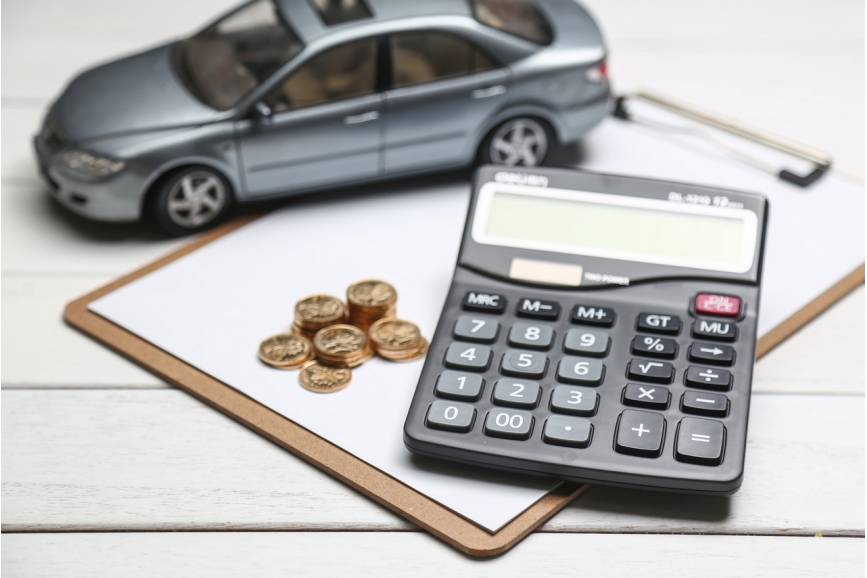 Zdjęcie przedstawia leżący na stole arkusz papieru, kalkulator, drobne monety i miniaturowy samochód